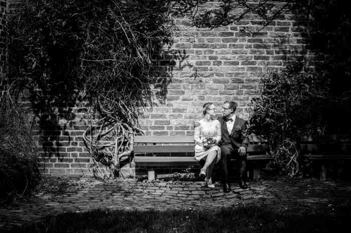 Brautpaar sitzt auf Bank vor Backsteinwand fotografiert von Studio Lüdeking Lüneburg