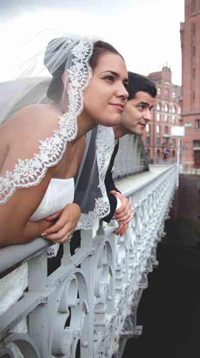 Hochzeitspaar schaut von einer Brücke an das Geländer gelehnt. Hochzeitsfoto in der Hamburger Speicherstadt. 