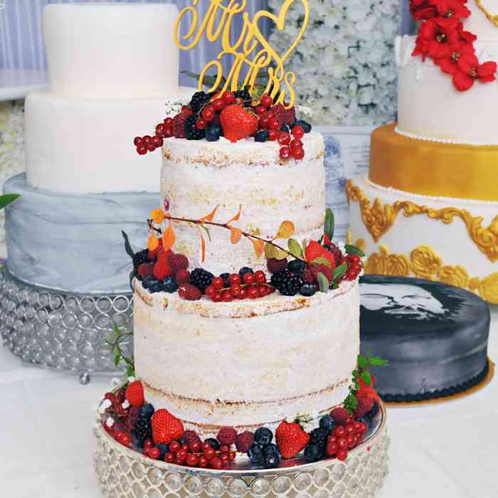 Die zweistöckige Hochzeitstorte ist mit frischen Früchten und Puderzucker dekoriert. 
