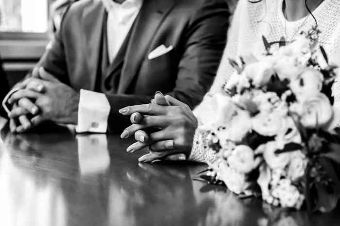 Brautpaar am Tisch des Standesbeamten mit gefalteten Händen.