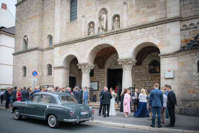Hochzeitsgesellschaft und Hochzeitsauto vor er Kirche.